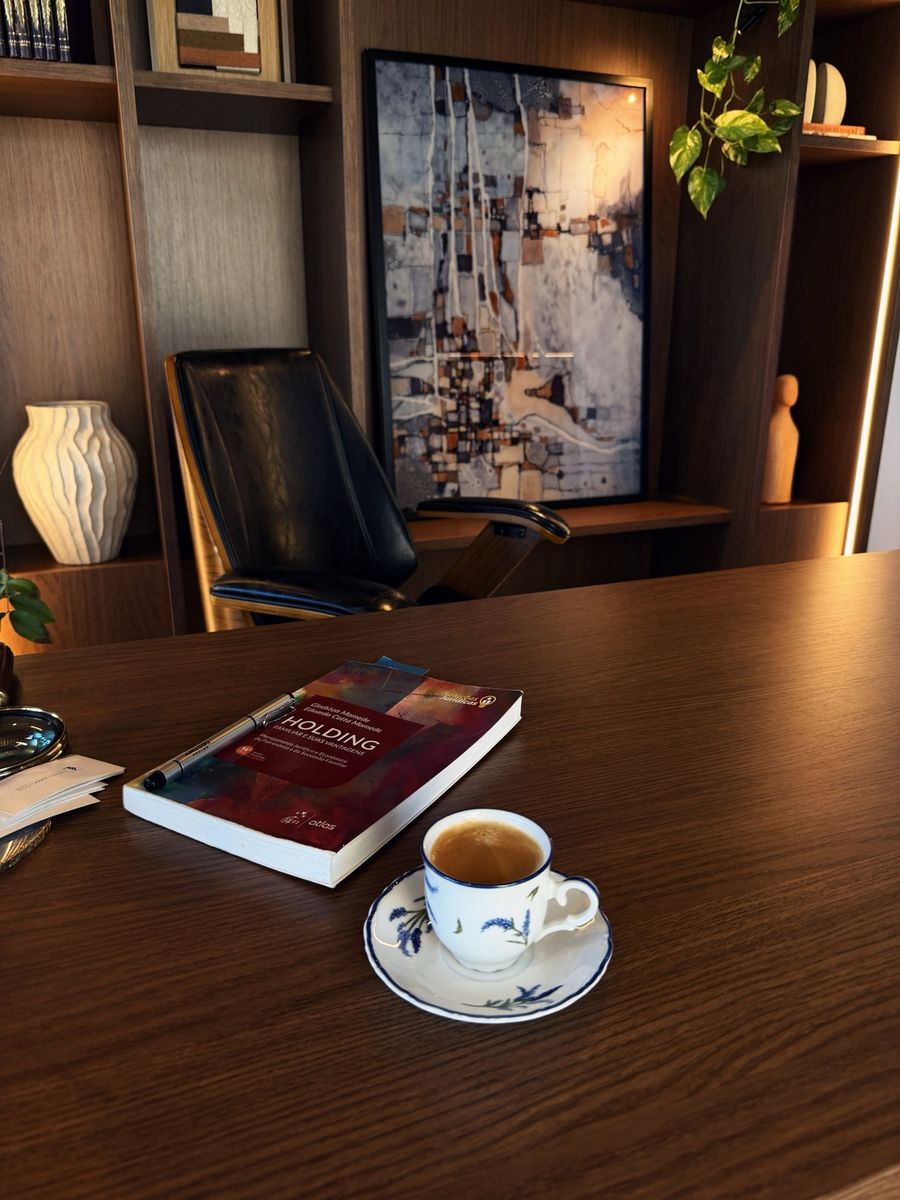Mesa de trabalho com um livro sobre holding e uma xícara de café